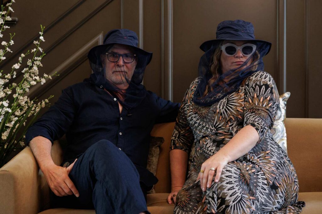 Mark and Amanda sitting on orange sofa being silly with beekeeper hats